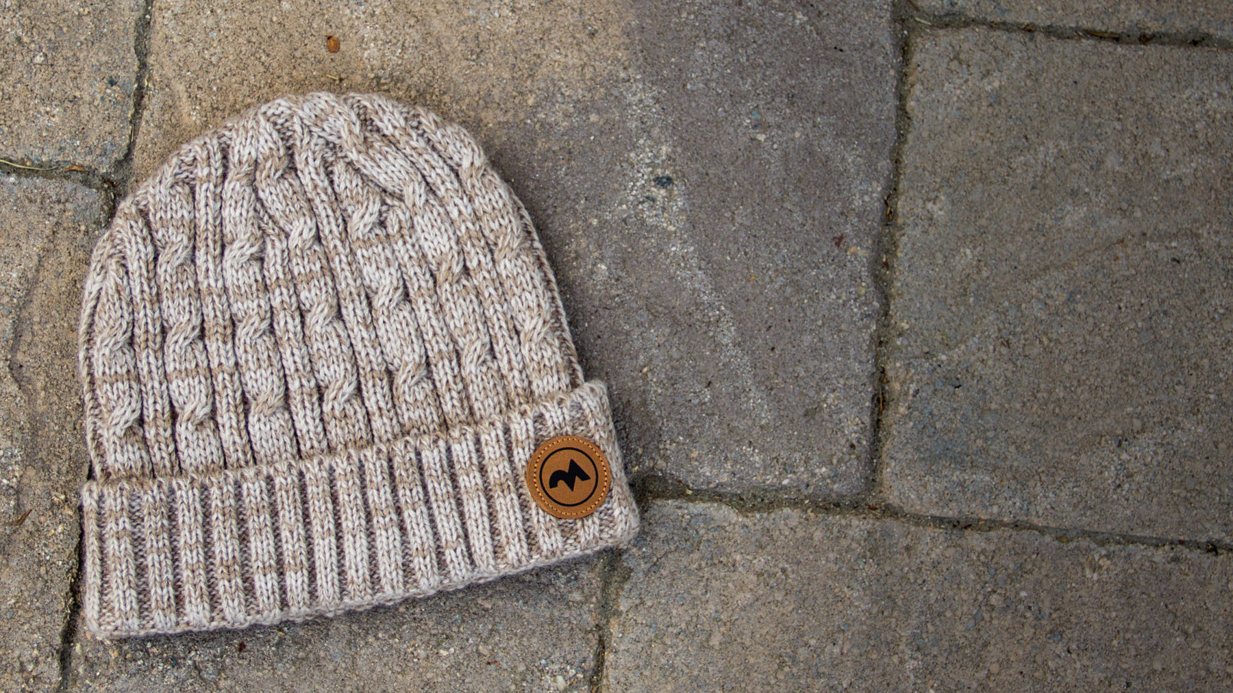 Cuffed Cable Knit hat laying on stone walkway